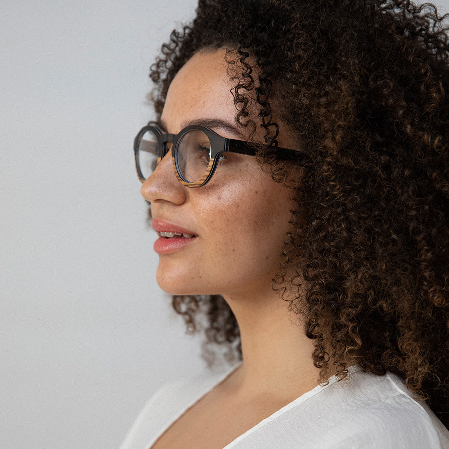 Black woman wearing round wooden glasses for optical lenses facing sideways