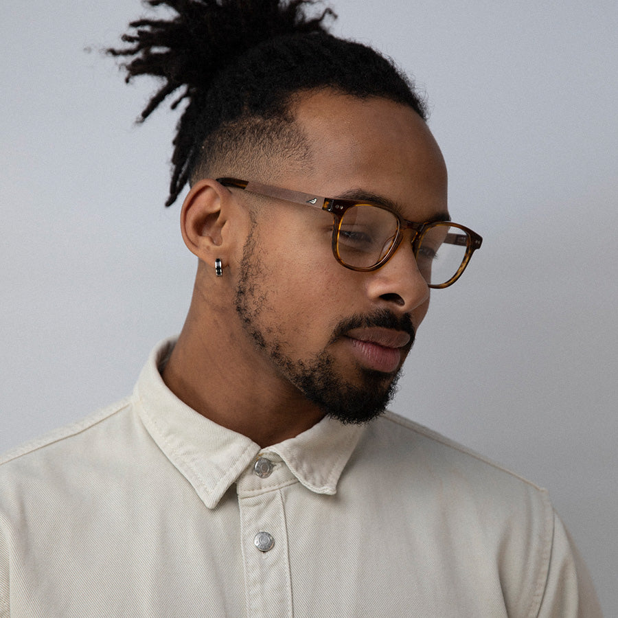 Black man wearing caramel rectangle small glasses  looking down