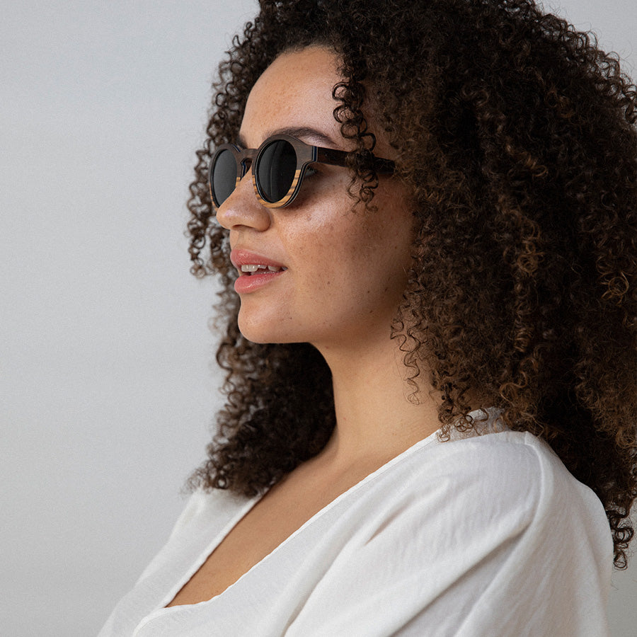 Black woman wearing eco friendly round wooden sunglasses with polarised lenses facing sideways