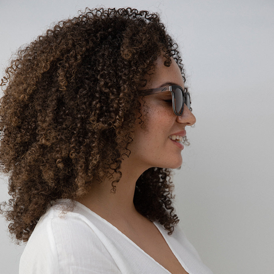Woman with frizzy hair wearing black and red wooden sunglasses looking sideways